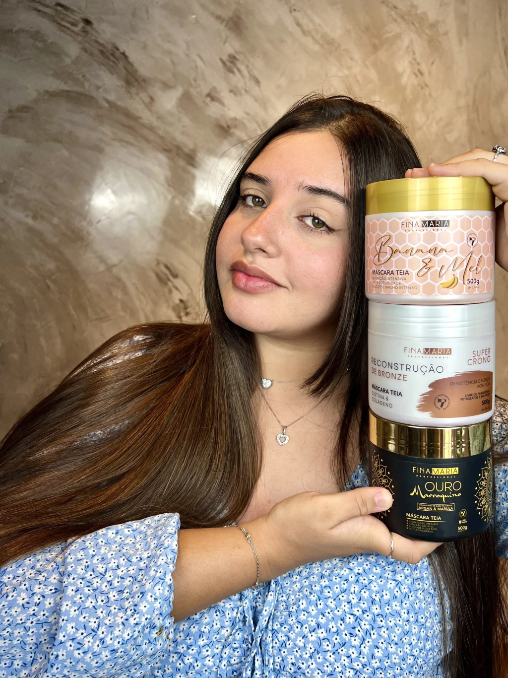 Cliente com cabelo longo e brilhante segurando as três máscaras Fina Maria